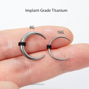 Peut inclure: Deux bijoux de corps en titane de qualit&eacute; implantaire en forme de croissant. L'un est &eacute;tiquet&eacute; 8G, l'autre 16G. Chaque pi&egrave;ce a un anneau en caoutchouc noir. Le texte "Implant-Grade Titanium" est au-dessus.