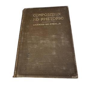 May include: A well-worn, brown hardcover book with the title "Composition and Rhetoric" and the authors Lockwood and Emerson. The cover has a textured finish and gold lettering. The book shows signs of age.