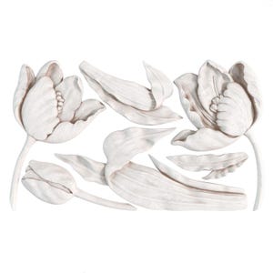 May include: A collection of white tulip flower sculptures and detached petals. The sculptures are detailed with textured surfaces and realistic forms. The arrangement includes open blooms, closed buds, and individual leaves.