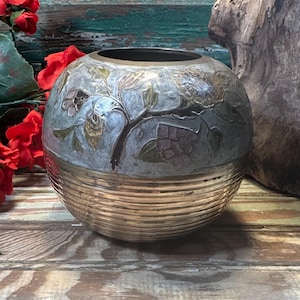 May include: A round brass vase with a silver and gold floral design. The vase has a textured bottom half.