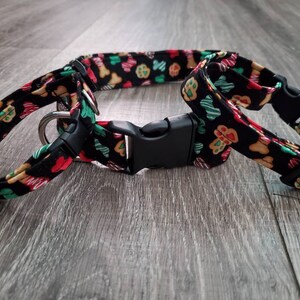 Puede incluir: Un collar de perro negro con un patr&oacute;n de galletas de jengibre y huellas de patas. El collar tiene una hebilla de pl&aacute;stico negro y un anillo en D plateado.