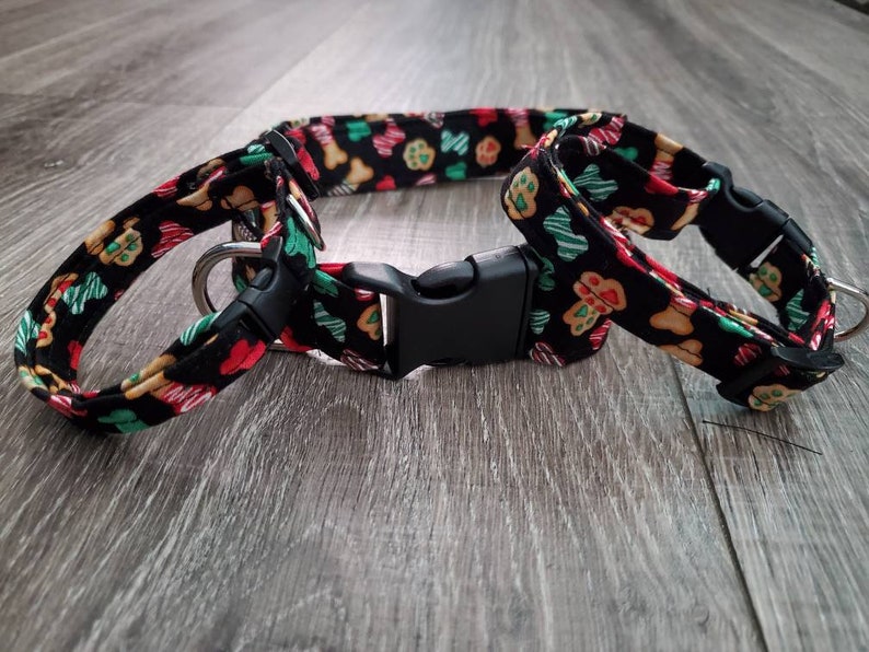 Puede incluir: Un collar de perro negro con un patr&oacute;n de galletas de jengibre y huellas de patas. El collar tiene una hebilla de pl&aacute;stico negro y un anillo en D plateado.