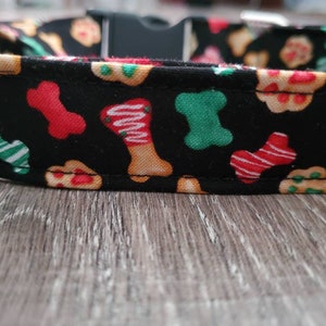 Puede incluir: Collar de perro negro con un patr&oacute;n festivo de galletas con forma de hueso rojas, verdes y blancas.