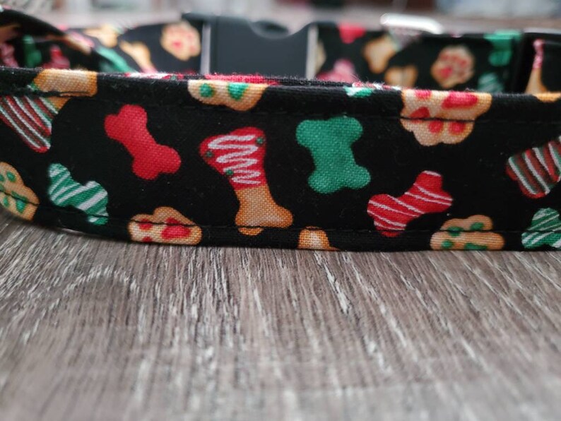 Puede incluir: Collar de perro negro con un patr&oacute;n festivo de galletas con forma de hueso rojas, verdes y blancas.
