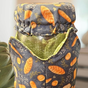 May include: A gray fabric jar cover with a green lining and orange and brown bread print. The text on the cover reads "At least we have each other" and "You can try me".