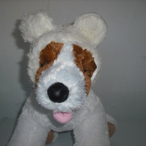 May include: White plush dog toy with brown ears and a white fur coat. The dog is wearing a white plush bear hat with floppy ears.