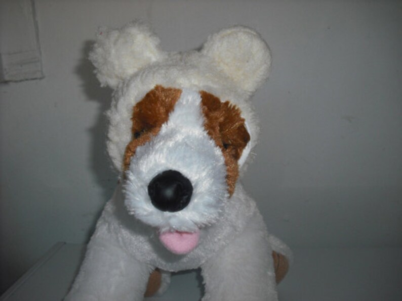 May include: White plush dog toy with brown ears and a white fur coat. The dog is wearing a white plush bear hat with floppy ears.