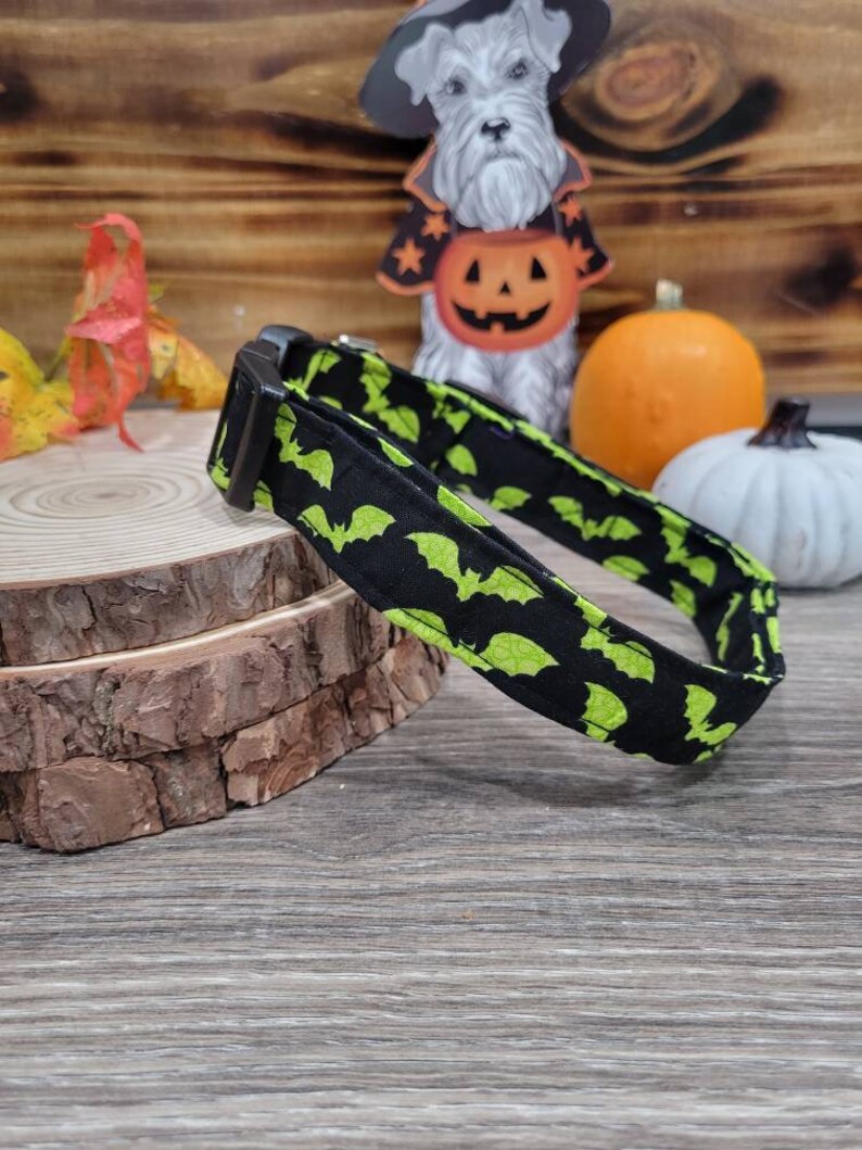 May include: A black and green dog collar with a bat pattern. The collar is made of fabric and has a black buckle.