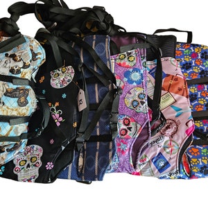 May include: Six different dog harnesses with various colorful patterns, including skulls, paw prints, and travel-themed designs. The harnesses are made of fabric and have adjustable straps.
