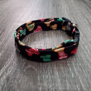 Puede incluir: Un collar ajustable negro con un patr&oacute;n de galletas de jengibre en rojo, verde y marr&oacute;n.