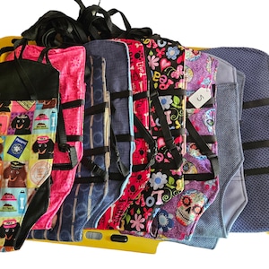 May include: A collection of colorful dog harnesses with various patterns, including a dachshund print, a floral print, and a skull print. The harnesses have adjustable straps and are made of durable fabric.