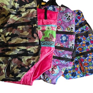 May include: Four different fabric dog harnesses with various patterns. The harnesses are made of a soft, durable fabric and feature adjustable straps for a comfortable fit. The patterns include camouflage, pink floral, purple skulls, and blue paw prints.