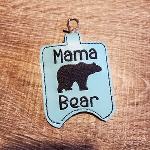 May include: A light blue leather keychain with a black bear silhouette and the text "Mama Bear" embroidered on it.