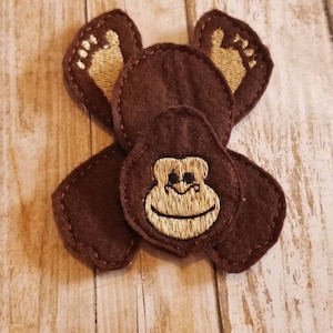 May include: A brown felt monkey applique with a gold embroidered face and feet. The monkey is made up of five separate pieces of felt.