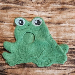 May include: Green felt frog puppet with embroidered eyes and a mouth. The puppet has a hole in the back for a hand to fit through.