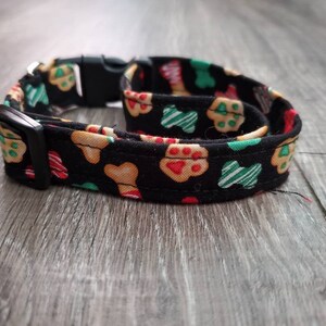 Puede incluir: Un collar de perro negro con un patr&oacute;n festivo de galletas de jengibre rojas, verdes y blancas, formas de hueso y huellas de patas.