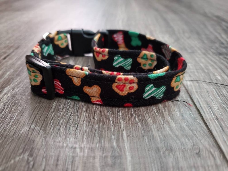 Puede incluir: Un collar de perro negro con un patr&oacute;n festivo de galletas de jengibre rojas, verdes y blancas, formas de hueso y huellas de patas.