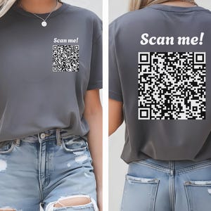 Könnte beinhalten: Ein graues T-Shirt mit dem Text "Scan me!" und einem schwarz-weißen QR-Code, der auf der Vorder- und Rückseite aufgedruckt ist.