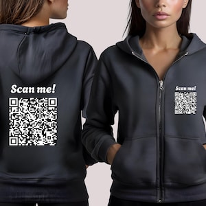 May include: Charcoal gray zip-up hoodie with a white "Scan me!" text and a QR code on the back and front. The hoodie has a hood, a zipper closure, and front pockets. The QR code is a black and white square.