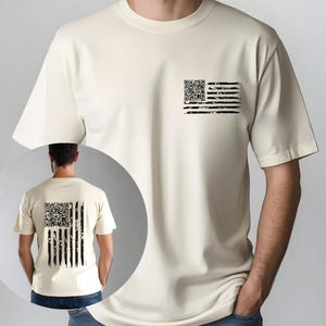 May include: Cream-colored t-shirt featuring a distressed black and white American flag design. The flag design is on the front left chest and the back of the shirt. The flag's stars are replaced with a QR code.