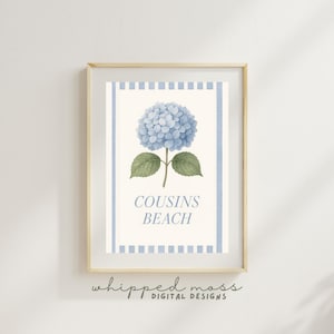 Puede incluir: Impresión enmarcada con una ilustración en acuarela de una flor de hortensia azul y hojas verdes. El texto "COUSINS BEACH" está debajo de la flor. El marco es de madera clara y el fondo es blanco.