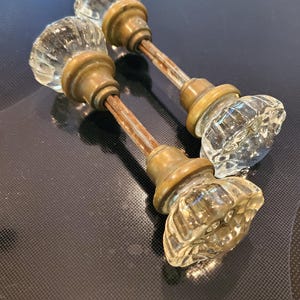 以下が含まれることがあります： 真鍮製のベースと摩耗したさびた金属シャフトが付いた、アンティークのガラス製のドアノブ2個