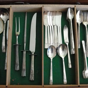 May include: A wooden drawer filled with silverware, including forks, spoons, knives, and serving utensils. The silverware is silver-colored and arranged on a green felt-lined surface. The drawer is open, showcasing the various pieces.