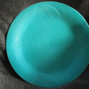 Puede incluir: Un plato de cerámica azul turquesa con un diseño decorativo. El plato tiene una superficie texturizada y un borde ligeramente elevado.