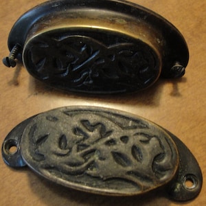 May include: Two antique brass cabinet pulls with an ornate floral design. The pulls are oval shaped and have a dark patina.