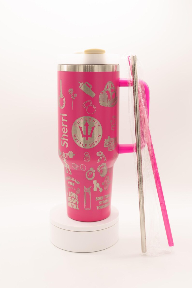 Pu&ograve; includere: Un bicchiere termico rosa con manico e cannuccia argentata. Il bicchiere &egrave; decorato con varie icone legate al fitness e il testo "Sherri" e "CrossFit Myrtle Beach". Un involucro di plastica trasparente copre la cannuccia.