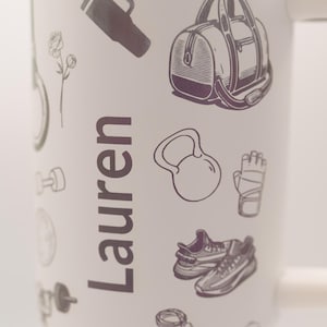 Pu&ograve; includere: Tazza da viaggio bianca con bordo arcobaleno e il nome "Lauren" stampato verticalmente. La tazza &egrave; decorata con illustrazioni di attrezzature per il fitness, tra cui una borsa da palestra, un kettlebell e scarpe da ginnastica.
