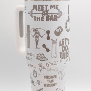 Pu&ograve; includere: Bicchiere termico bianco con manico e coperchio. Il bicchiere &egrave; decorato con grafiche e testo a tema fitness, tra cui "Meet Me at the Bar", una donna che salta la corda, manubri e la frase "Let's Do This".