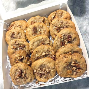 May include: A white box filled with pecan cookies. The cookies are golden brown and have a crispy texture. The box is lined with white paper.