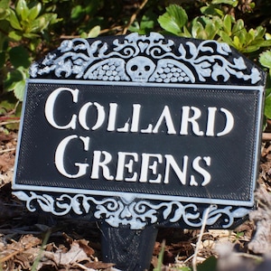 May include: Black garden marker with white lettering that reads "COLLARD GREENS". The marker has a decorative top with a skull and wings.