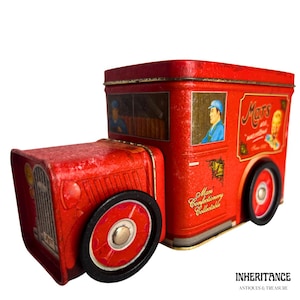 Könnte beinhalten: Eine rote Mars-Konfekt-Truck-Blechdose im Vintage-Stil mit schwarzen Rädern und goldenen Akzenten. Die Dose zeigt Illustrationen von Personen in den Fenstern und das Mars-Logo. Auf der Seite steht "Mars Confectionery Collectable".