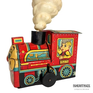 May include: A red, blue, and yellow wind-up toy train with a smiling face and a cartoon engineer in the cab. The train has a white smoke stack and the number 5271 on the side.