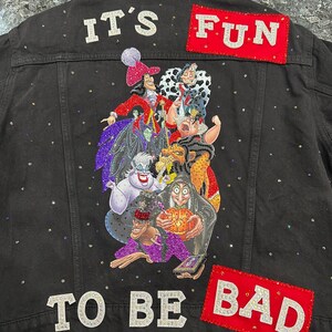 May include: Black denim jacket with a colorful graphic of Disney villains on the back. The jacket has the phrases "IT'S FUN" and "TO BE BAD" in sparkly letters and patches. Small rhinestones are scattered across the jacket.