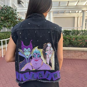 May include: Black denim vest with a colorful graphic of Disney villains Maleficent, Ursula, and Cruella de Vil. The vest is embellished with rhinestones and the word "VILLAINS" in purple letters.