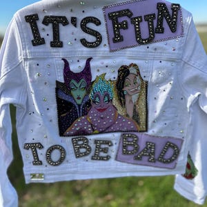May include: White denim jacket with a purple, green, and blue cartoon image of three Disney villains. The jacket has rhinestones and the text "It's Fun To Be Bad" in black.