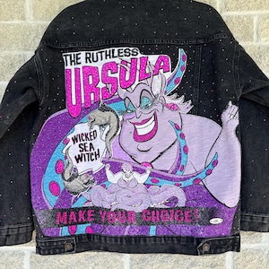 May include: A black denim jacket featuring a large graphic of the character Ursula on the back. The design includes the text THE RUTHLESS URSULA, WICKED SEA WITCH, and MAKE YOUR CHOICE! The jacket is embellished with small sparkling rhinestones.