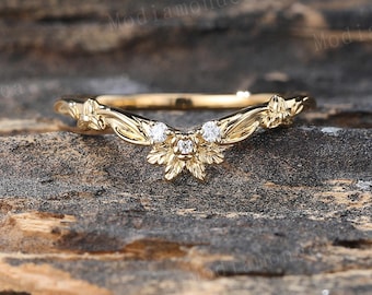 May include: A delicate gold wedding band with a V-shaped design featuring intricate floral details and small diamonds.