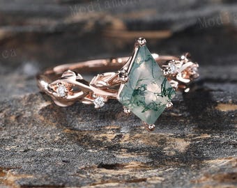Puede incluir: Un anillo de compromiso de oro rosa con una piedra preciosa de ágata verde musgo y pequeños diamantes engastados en un delicado diseño de vid.
