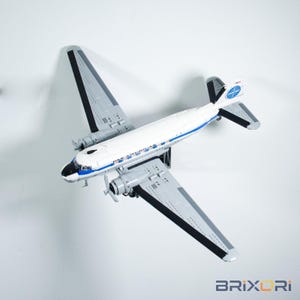 May include: A model airplane constructed from building blocks, featuring a white fuselage with a blue stripe and the text PAN AMERICAN. The wings are grey with black accents, and the tail fin displays the blue and white Pan American globe logo.