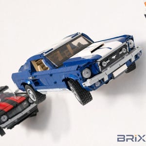 May include: A blue and white brick-built model car featuring a Mustang emblem on the front grille, a tan interior, and black tires. The vehicle is mounted on a wall alongside a black and red brick-built car model and a partial white vehicle.