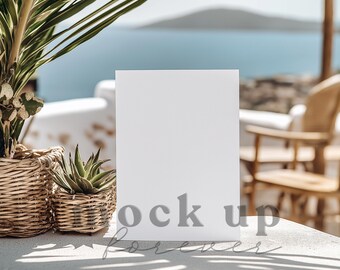 May include: A white blank sign mockup on a white table with a potted succulent plant and a palm leaf in the background. The sign is sitting on a white table with a blurred background of a beach and a chair.