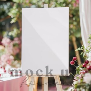 Op de afbeelding: Een wit leeg bord op een ezel met een houten frame. Het bord staat voor een roze bloemstuk en een wit gordijn.