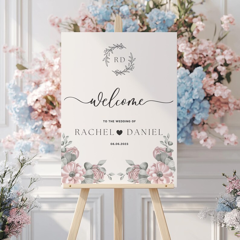 May include: A white welcome sign with a floral design and the text "Welcome to the wedding of Rachel & Daniel 08.06.2023".