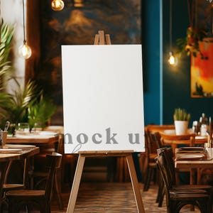 Könnte beinhalten: Eine leere weiße Leinwand auf einem Staffelei in einem Restaurant. Die Leinwand befindet sich in der Mitte des Bildes und ist von Tischen und Stühlen umgeben. Die Leinwand ist bereit für ein Schild oder ein Kunstwerk.