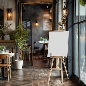 Op de afbeelding: Een houten ezel met een leeg wit doek, staand in een restaurant. De ezel staat op de voorgrond, met een tafel en stoelen op de achtergrond.