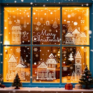 Op de afbeelding: Een raam versierd met witte kerstthema-stickers. Het ontwerp omvat huizen, sneeuwvlokken, kerstbomen, ornamenten en de tekst "Merry Christmas". Het raam is blauw omlijst en heeft een warme, uitnodigende gloed.